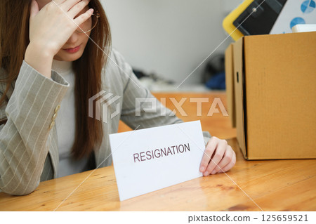 Unemployed woman with resignation letter and office box showing stress after layoff 125659521
