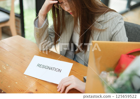 Unemployed woman with resignation letter and office box showing stress after layoff 125659522