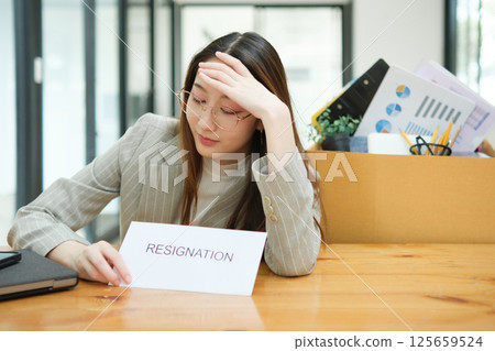 Unemployed woman with resignation letter and office box showing stress after layoff Unemployed woman with resignation letter and office box showing stress after layoff 125659524