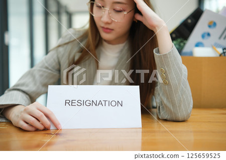 Unemployed woman with resignation letter and office box showing stress after layoff 125659525