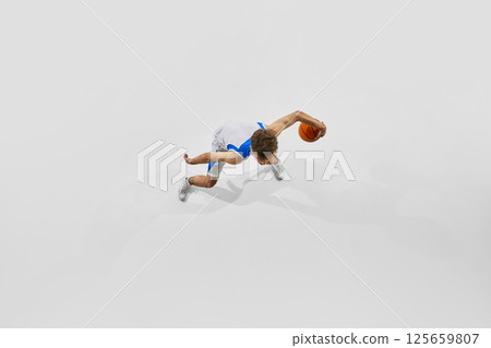 Top view photo of male basketball athlete dribbling ball fast ad low against white studio background. Dribbling technique training. Top view photo of male basketball athlete dribbling ball fast ad low against white studio background. Dribbling technique training. 125659807