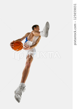 Low angle dynamic phot of basketball player charging forward with intensity, eyes on goal, gripping ball, wearing blue-white uniform against white background. Low angle dynamic phot of basketball player charging forward with intensity, eyes on goal, gripping ball, wearing blue-white uniform against white background. 125659831