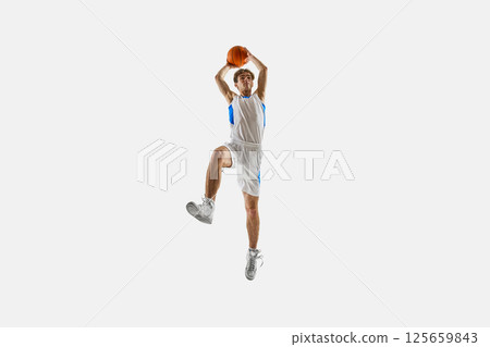 Focused player captured in high leap holds ball overhead ready to strike, full intensity in motion against white background. Focused player captured in high leap holds ball overhead ready to strike, full intensity in motion against white background. 125659843