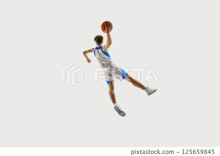 Peak tension moment. Basketball player flying backward in twisting leap, hand stretched up gripping ball against white background. 125659845