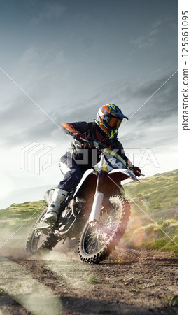 Vertical image of bike rider leans forward accelerating on dusty grassy path with sun flares and scenic view. Off road travel. Composite image Vertical image of bike rider leans forward accelerating on dusty grassy path with sun flares and scenic view. Off road travel. Composite image 125661095