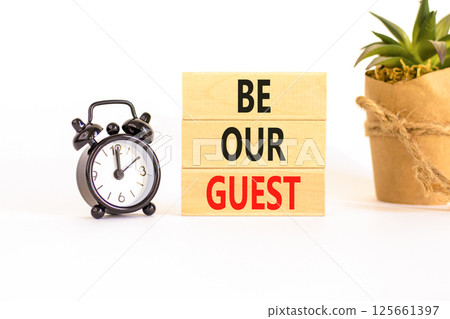 Be our guest symbol. Concept words Be our guest on beautiful wooden block. Black alarm clock. Beautiful white background. Business and be our guest concept. Copy space. 125661397