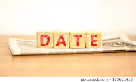 Date symbol. Concept word Date on beautiful wooden blocks on newspaper. Beautiful wooden table white background. Business and date concept. Copy space. Date symbol. Concept word Date on beautiful wooden blocks on newspaper. Beautiful wooden table white background. Business and date concept. Copy space. 125661438