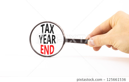 Tax year end symbol. Concept words Tax year end on beautiful black magnifying glass. Beautiful white background. Businessman hand. Business tax year end concept. Copy space. 125661536