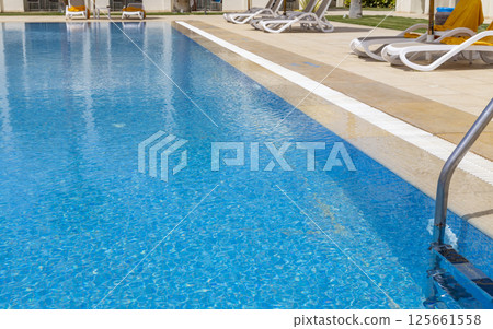 Summer seaside relax mood travel vacation a luxurious pool hotel interior for a summer holiday in warm countries. Beautiful tropical beach hotel resort with swimming pool, sun loungers palm trees 125661558