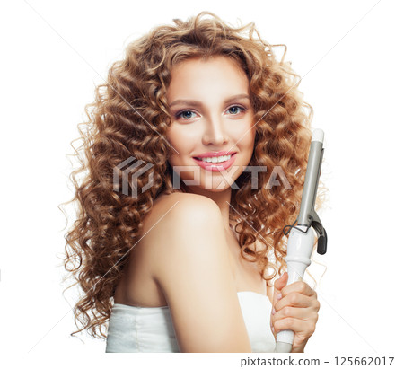 Indoor portrait of young model woman with long curly wavy hairstyle showing hot curling tongs iron 125662017