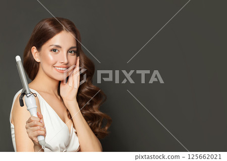 Stylish young model woman with long curly wavy hairstyle showing hot curling tongs iron Stylish young model woman with long curly wavy hairstyle showing hot curling tongs iron 125662021