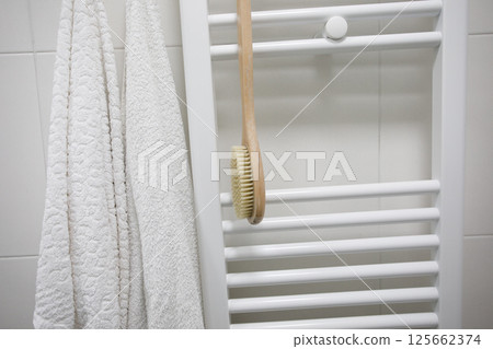 White bathroom interior detail. Heated towel rail with white cotton towel and brush 125662374