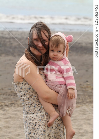 Cute mother embracing her daughter baby girl at the sea beach. Young woman and child one year old Cute mother embracing her daughter baby girl at the sea beach. Young woman and child one year old 125662453