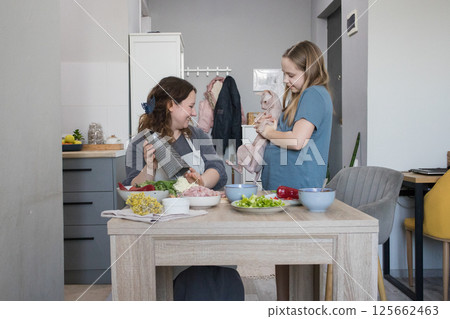 Cute family. Adult mother, young daughter and funny cat having fun together at domestic kitchen 125662463