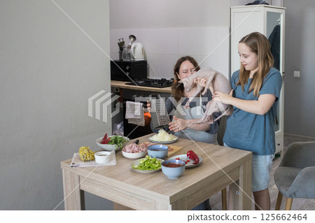 Cheerful family. Adult mother, young daughter and funny cat having fun together at domestic kitchen 125662464