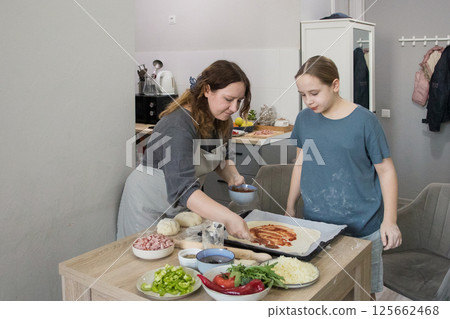 Happy daughter cooking pizza with her mother in the kitchen Happy daughter cooking pizza with her mother in the kitchen 125662468