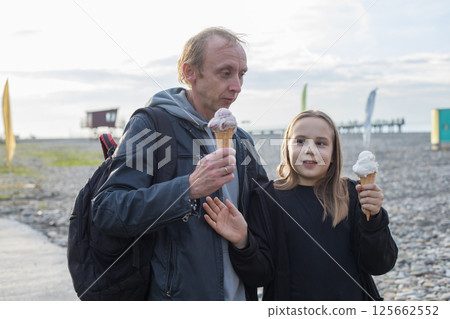 Laughing child daughter and her father walking and eating ice cream outdoors. Happy family Laughing child daughter and her father walking and eating ice cream outdoors. Happy family 125662552