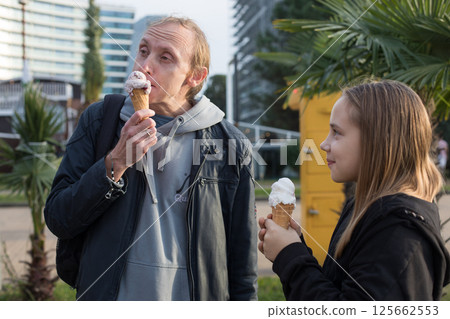 Smiling child daughter and her father walking and eating ice cream outdoors. Happy family 125662553
