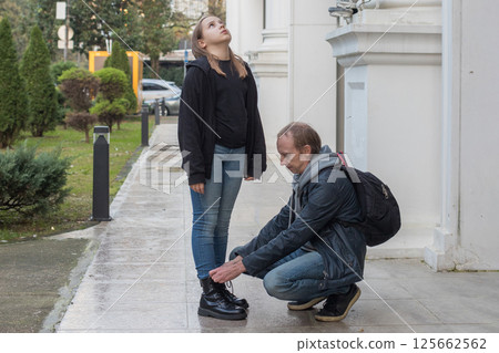 Father helping his daughter tie her shoelace outdoors 125662562