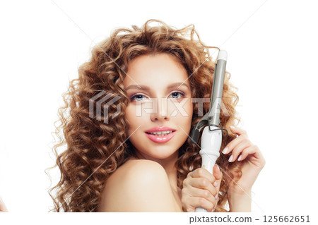 Cheerful young model woman with long curly wavy hairstyle showing hot curling tongs iron 125662651