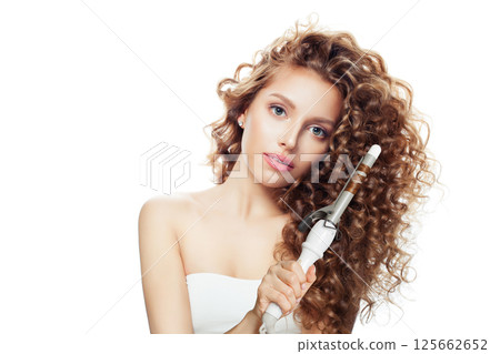 Isolated young model woman with long curly wavy hairstyle showing hot curling tongs iron 125662652