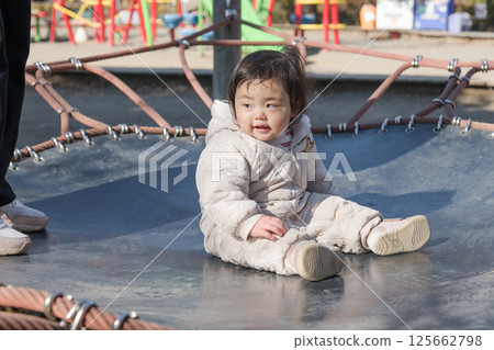 [A one-year-old child playing with his mother on the trampoline in the children's playground at Sagamihara City Asamizo Park] 125662798