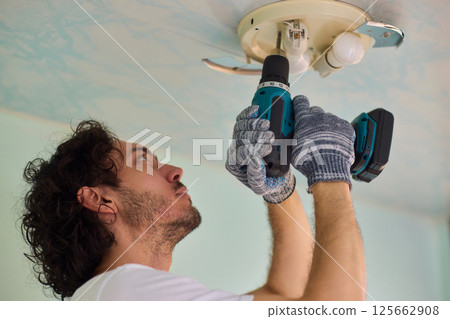 A person is installing a ceiling light fixture using a power tool with great care and skill A person is installing a ceiling light fixture using a power tool with great care and skill 125662908