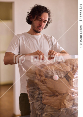 A man is unpacking clothes carefully from a bag while situated in a bright and inviting room A man is unpacking clothes carefully from a bag while situated in a bright and inviting room 125663184
