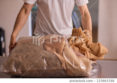 A man is unpacking clothes carefully from a bag while situated in a bright and inviting room A man is unpacking clothes carefully from a bag while situated in a bright and inviting room 125663198