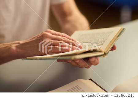 Hands purposefully engaged with an engrossing book carefully placed on a table surface 125663215