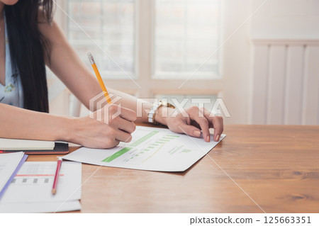 Close up of asian woman hand holding pencil analysis the graph at the home office for setting challenging business goals And planning to achieve the new target. Close up of asian woman hand holding pencil analysis the graph at the home office for setting challenging business goals And planning to achieve the new target. 125663351
