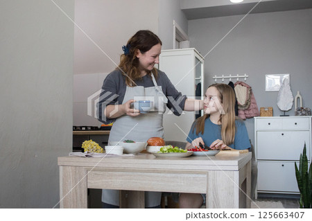 Happy mother and daughter preparing tasty food at kitchen. Mommy teaching lovely kid to cook Happy mother and daughter preparing tasty food at kitchen. Mommy teaching lovely kid to cook 125663407