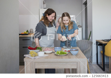 Mid adult mother and young daughter preparing tasty food at kitchen. Family together. Mid adult mother and young daughter preparing tasty food at kitchen. Family together. 125663413