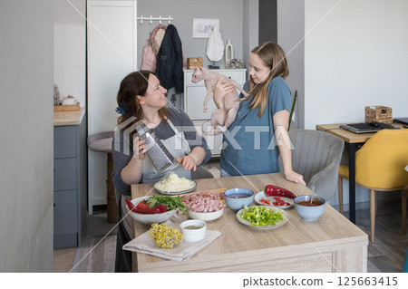 Happy family. Adult mother, young daughter and funny cat having fun together at domestic kitchen 125663415