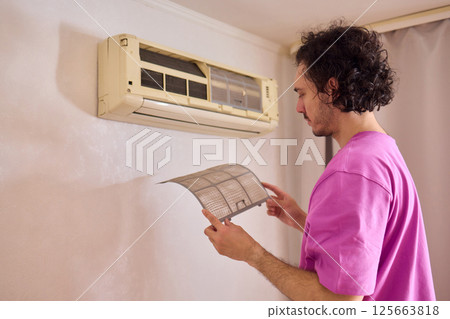A person is diligently inspecting the filter of an air conditioning unit for optimal performance 125663818