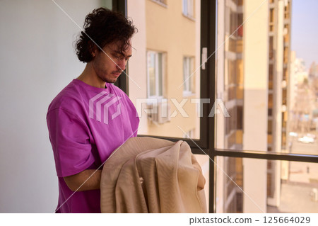 A Young Man Holding a Soft Blanket by the Window, Highlighting His Carefree Spirit 125664029
