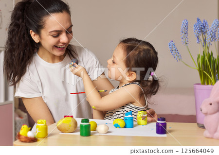 Happy mother and cute little child girl are preparing to celebrate Easter at home. Mom and daughter painting eggs before Easter together. Happy mother and cute little child girl are preparing to celebrate Easter at home. Mom and daughter painting eggs before Easter together. 125664049