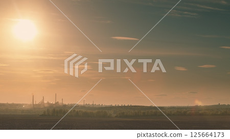 The stunning sunset casts a warm glow over an industrial landscape with a dynamic skyline 125664173