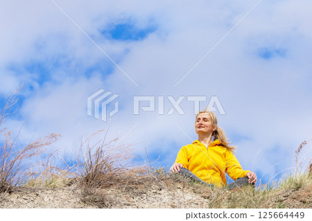 Woman is sitting on the hill and connecting with nature under the sky. 125664449