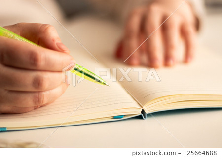 Warm toned image of hand writing personal thoughts in diary. Blurred background for cozy atmosphere. Warm toned image of hand writing personal thoughts in diary. Blurred background for cozy atmosphere. 125664688
