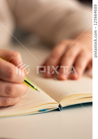 Side view of hand writing notes with pen in plain notebook. Minimalist workspace with natural lighting. Side view of hand writing notes with pen in plain notebook. Minimalist workspace with natural lighting. 125664689