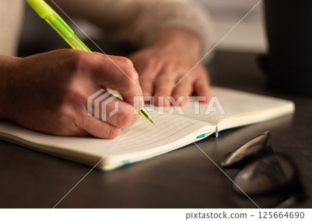 Close up image of human holding pen and writing something on blank white page in notebook. Close up image of human holding pen and writing something on blank white page in notebook. 125664690