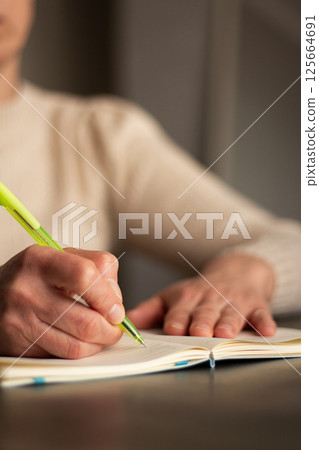 Warm toned image of hand writing personal thoughts in diary. Blurred background for cozy atmosphere. Warm toned image of hand writing personal thoughts in diary. Blurred background for cozy atmosphere. 125664691