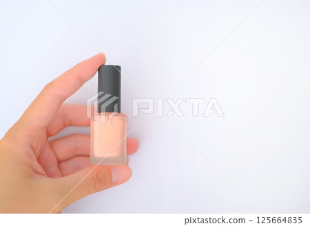 Close-up of a woman's hand holding a bottle of nude-colored nail polish with a matte black cap 125664835