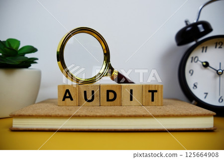 Magnifying glass and alarm clock with wooden blocks alphabet letters AUDIT text message on yellow background 125664908