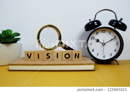 Magnifying glass and alarm clock with wooden blocks alphabet letters VISION text message on yellow background 125665021