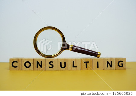 Magnifying glass with wooden blocks alphabet letters CONSULTING text message on yellow background 125665025