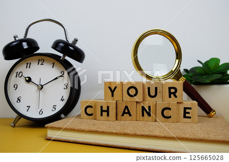 Magnifying glass and alarm clock with wooden blocks alphabet letters YOUR CHANCE text message on yellow background Magnifying glass and alarm clock with wooden blocks alphabet letters YOUR CHANCE text message on yellow background 125665028