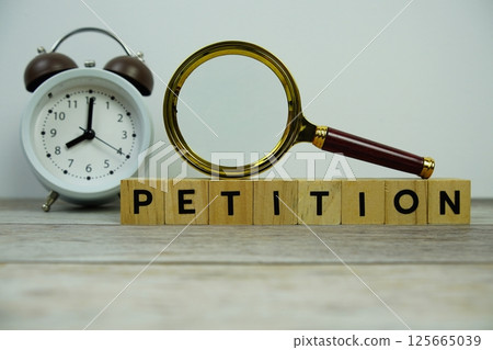 Magnifying glass and alarm clock with wooden blocks alphabet letters PETITION text message on wooden background 125665039