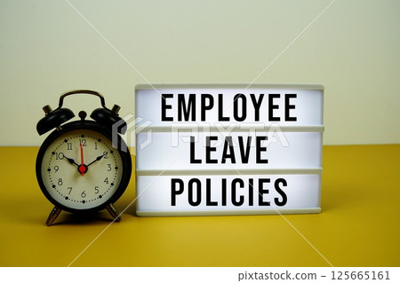 Employee Leave Policies text on light box with alarm clock on yellow background 125665161